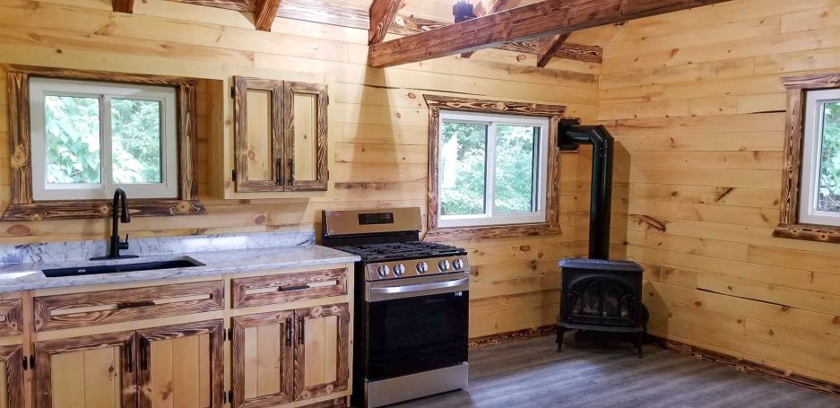 Wood cabin interior Kitchen with oven, wood stove, sink, and countertop.